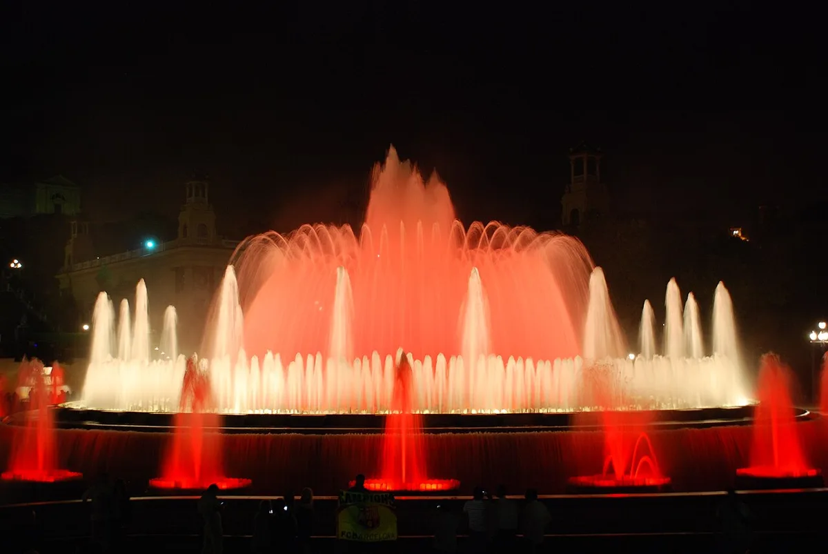 De Font Màgica de Montjuïc tijdens de avondshow met rode verlichtingsspiegeling en het Palau Nacional op de achtergrond